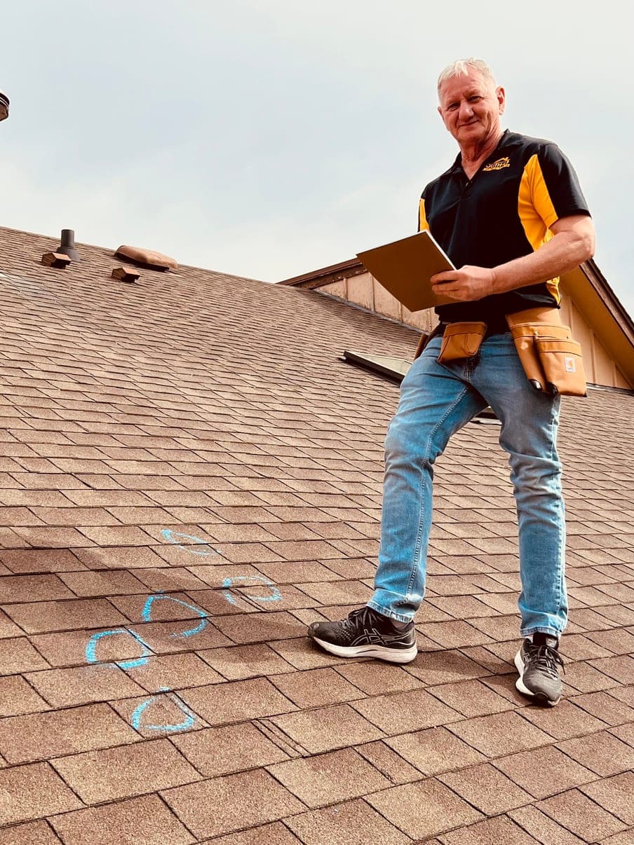 Byron Bothwell Sr., co-owner of South O Roofing, standing on a customer's roof in the Omaha metro with hail strikes circled in blue chalk